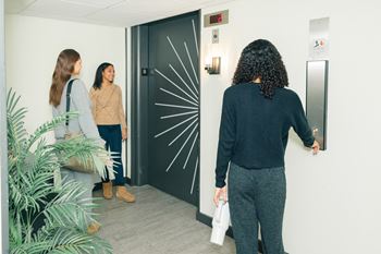 A woman with a white mug in her hand is entering a room through a black door at Walnut Towers at Frick Park, Pittsburgh