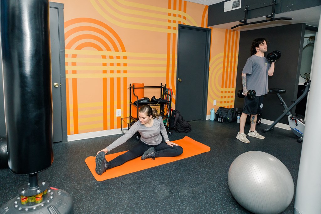 A man and a woman are exercising in a gym with orange and black accents at Walnut Towers at Frick Park, Pittsburgh