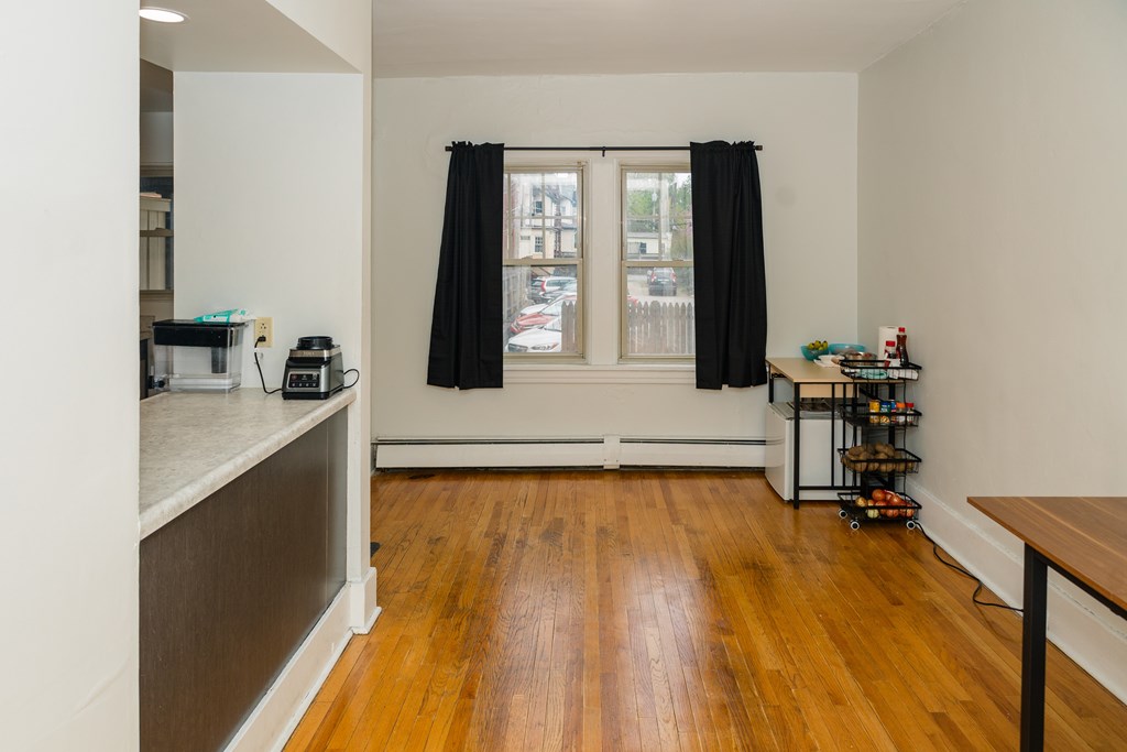 A kitchen with a wooden floor and a window with black curtains.