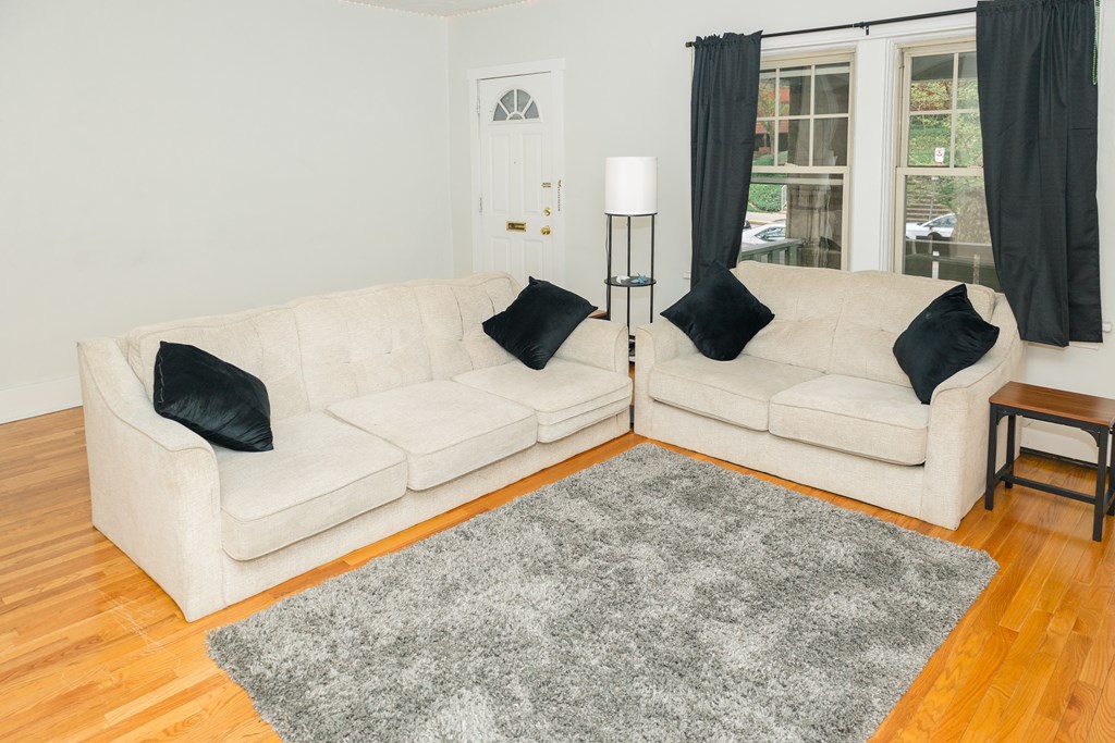 A white couch with black pillows sits in a room with a grey rug.
