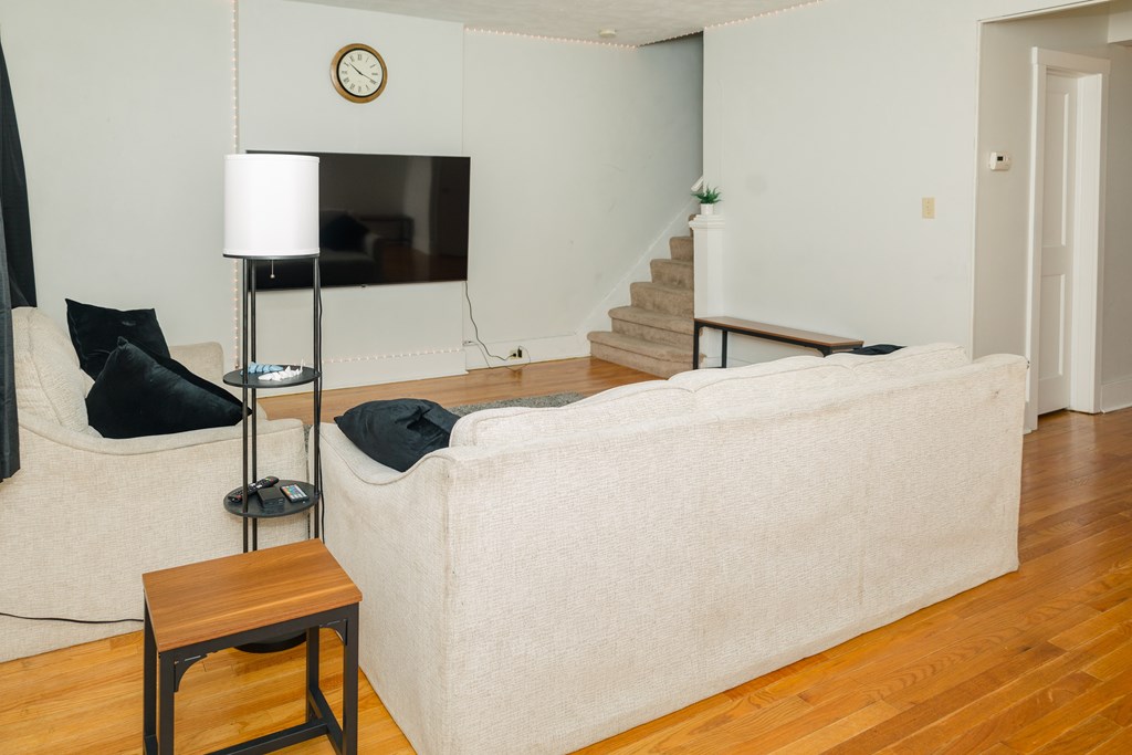 A living room with a white couch, a wooden stool, and a lamp.