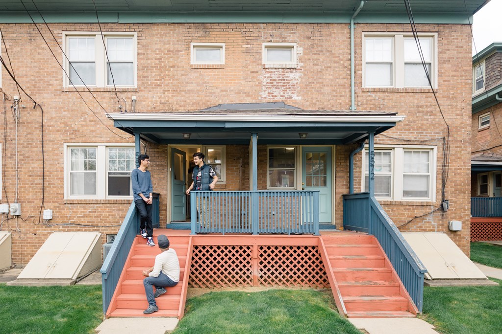 A man is sitting on the steps of a house while another man stands on the porch.