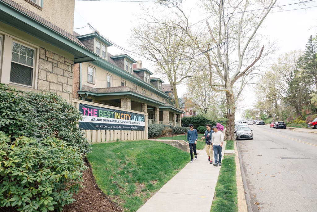 Three people walking down a sidewalk past a sign that says "The Best In City Living".