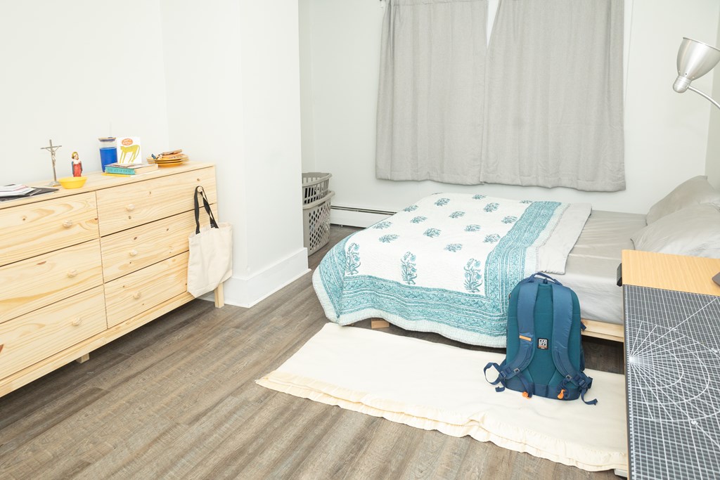 A bedroom with a bed, a dresser, and a backpack on the floor.