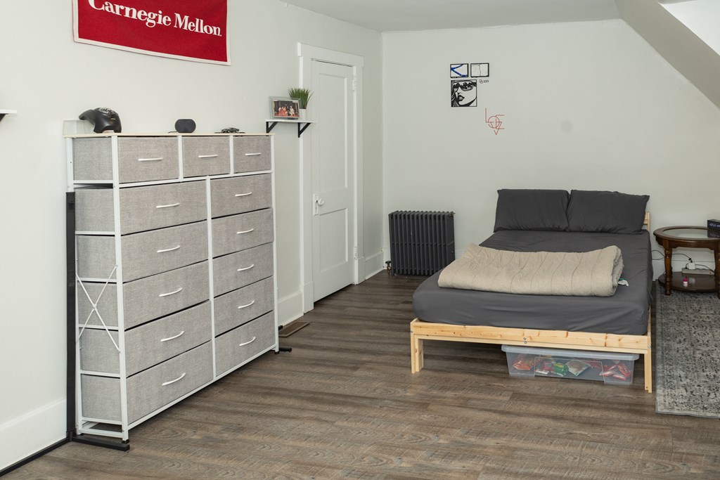 A bedroom with a bed, dresser, and a sign that says "Carnegie Mellon" on the wall.