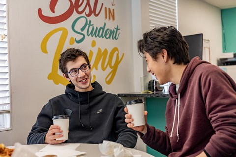 two students sitting at a table in front of a sign that says best in student living at University Commons Apartments, Oakland, Pittsburgh