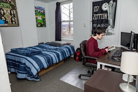a student sits at a desk in a dorm room with a bed in the background at University Commons Apartments, Oakland, Pittsburgh