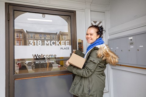 a woman standing in front of a door with a cardboard box in her hand at University Commons Apartments, Oakland, Pittsburgh