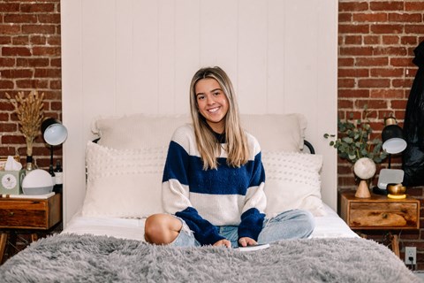 a woman sitting on a bed with a brick wall behind her at University Commons Apartments, Oakland, Pittsburgh