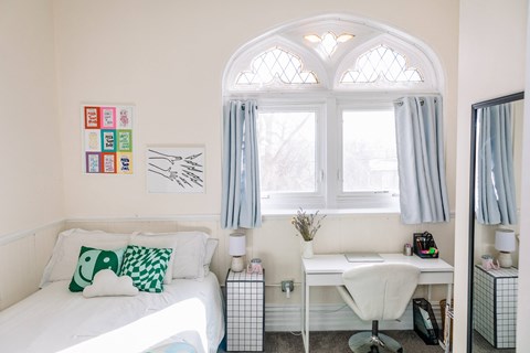 a bedroom with a white bed with green and white pillows and a white desk at University Commons Apartments, Oakland, Pittsburgh