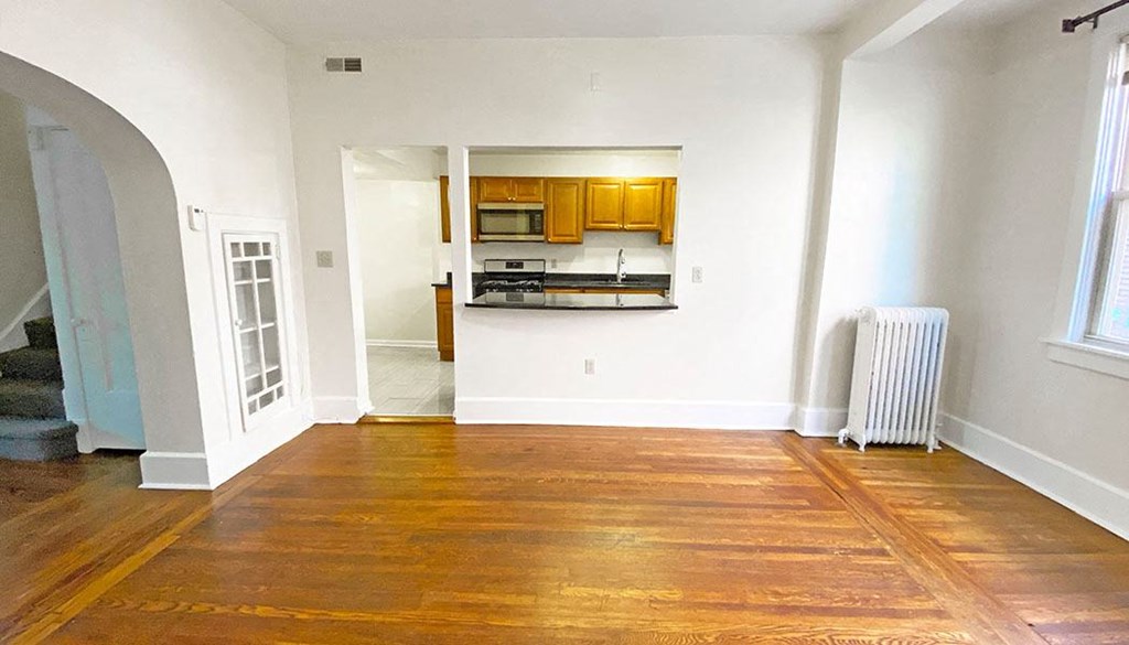 an empty living room with a kitchen in the background