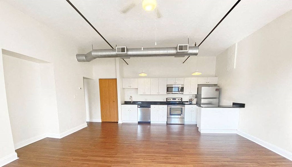 an empty living room with a kitchen in the background
