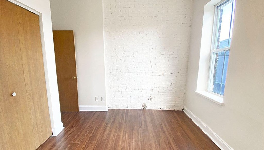 an empty room with a wooden floor and a brick wall