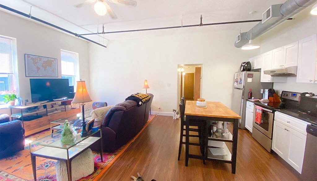 a living room with a couch a table and a kitchen with a stove and refrigerator