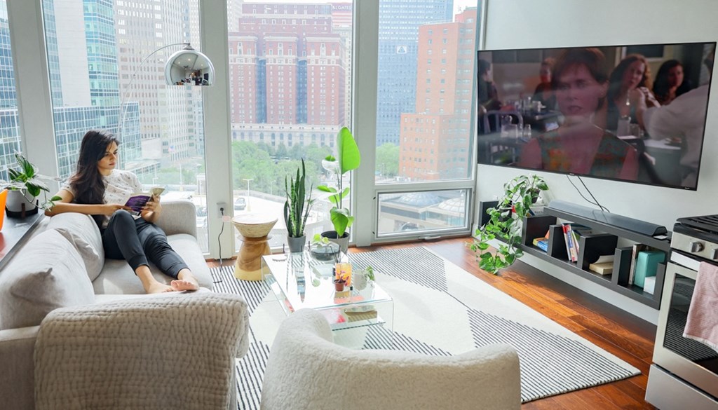 a woman sitting on a couch in a living room with a large tv in front of her at The Washington at Chatham, Pennsylvania, 15219