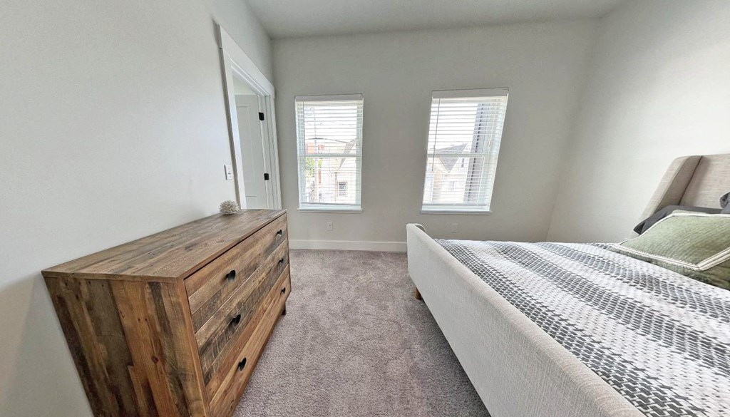 a bedroom with a bed and a dresser and two windows
