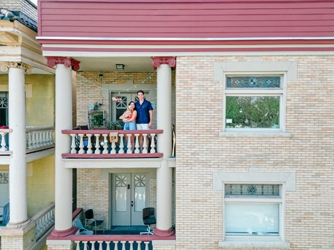 A couple is standing on a balcony of a two-story building.