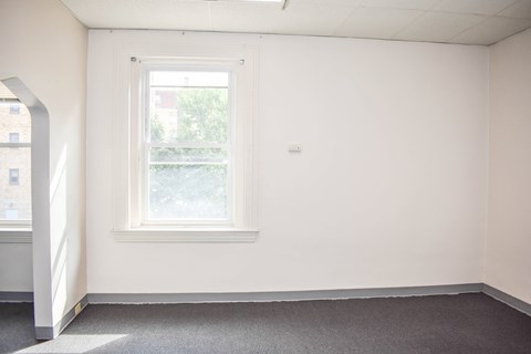 A room with a window and a grey carpet.