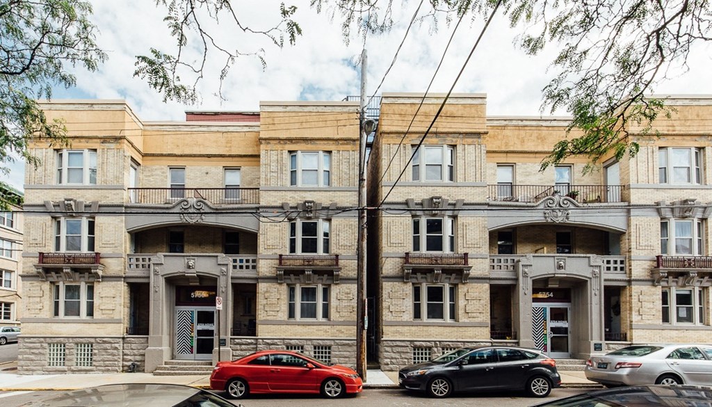 a three story apartment building on a city street with cars parked in front of it
