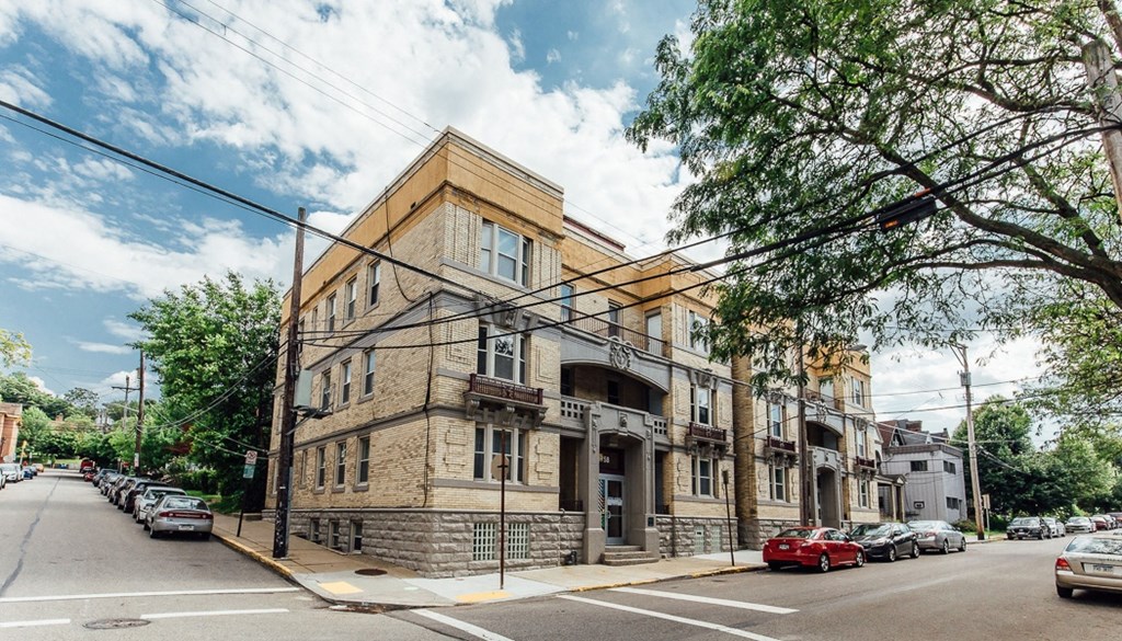 a three story brick building on a street corner with cars parked on the side of the road