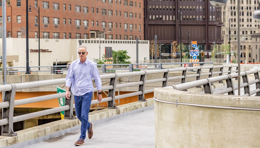 a man in a blue shirt and jeans walking across a bridge at The Washington at Chatham, Pittsburgh, PA 15219