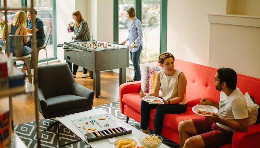 a group of people sitting in a living room next to a foosball table at Walnut on Highland, Pittsburgh, PA