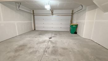 a white garage with a green trash can and a white door