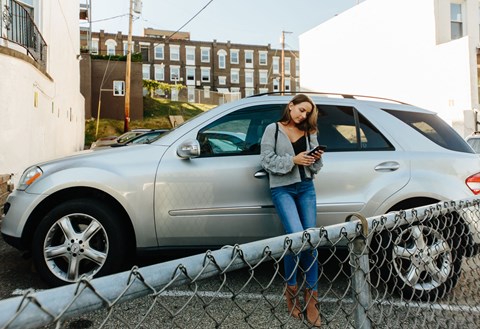 a woman leaning against a car looking at her phone at University Commons Apartments, Oakland, Pittsburgh
