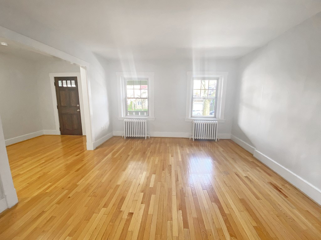 A room with wooden flooring and two windows.