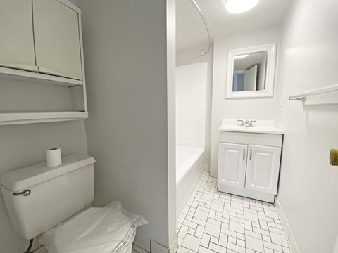 A white toilet with a toilet paper on top and a white trash bag on the floor.