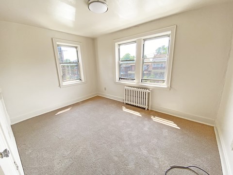 A room with a carpeted floor and two windows.