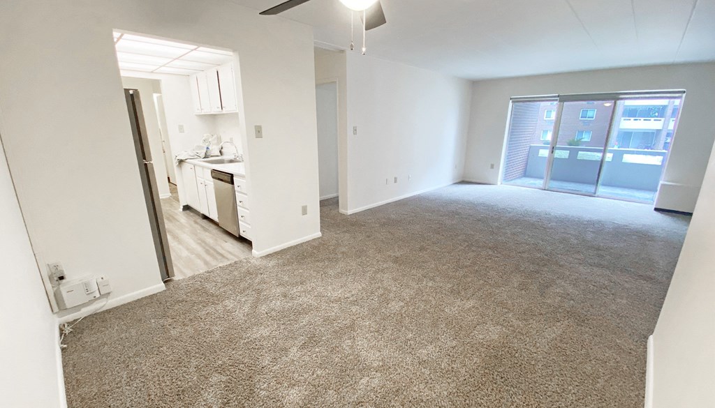 an empty living room with a kitchen in the background