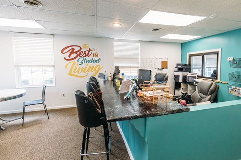 a desk with chairs and a counter in front of a wall with a sign that says best at University Commons Apartments, Oakland, Pittsburgh