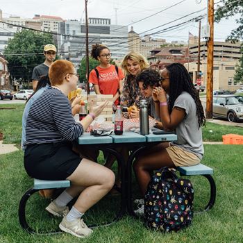 a group of people eating at a picnic table in a park at University Commons Apartments, Oakland, Pittsburgh