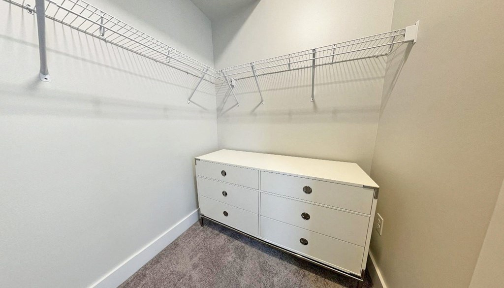 an empty closet with a white dresser and a wire rack