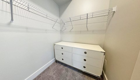 an empty closet with a white dresser and a wire rack