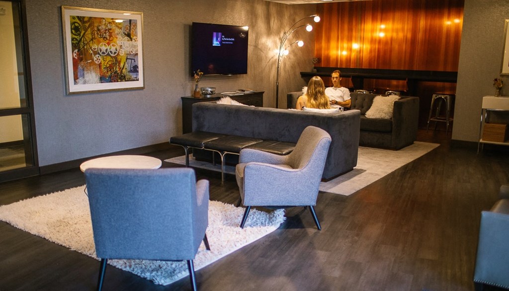 a couple sits on a couch in front of a tv in a hotel lobby