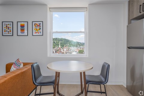 A dining room with a table and chairs and a window overlooking a city. at The Jones Tower at the Collective, Pittsburgh, PA 15203