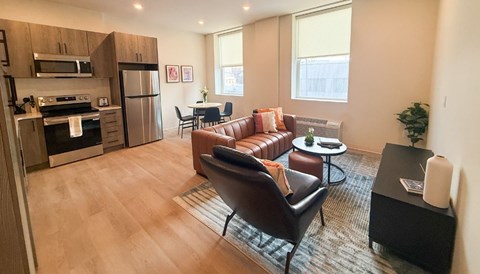 A modern kitchen and living room with a brown leather couch and a wooden floor.