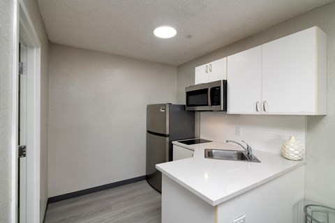 a white kitchen with a stainless steel refrigerator and microwave