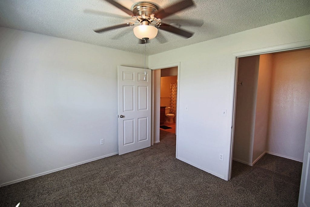 an empty living room with a ceiling fan and a door to a bathroom