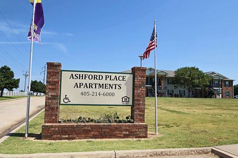 a sign place apartments in front of a lawn with two flags