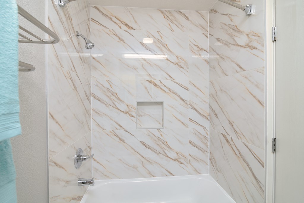 a white marble shower with a glass door and a white tub
