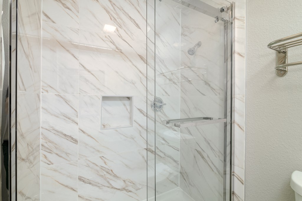 a shower with a glass door in a white marble bathroom