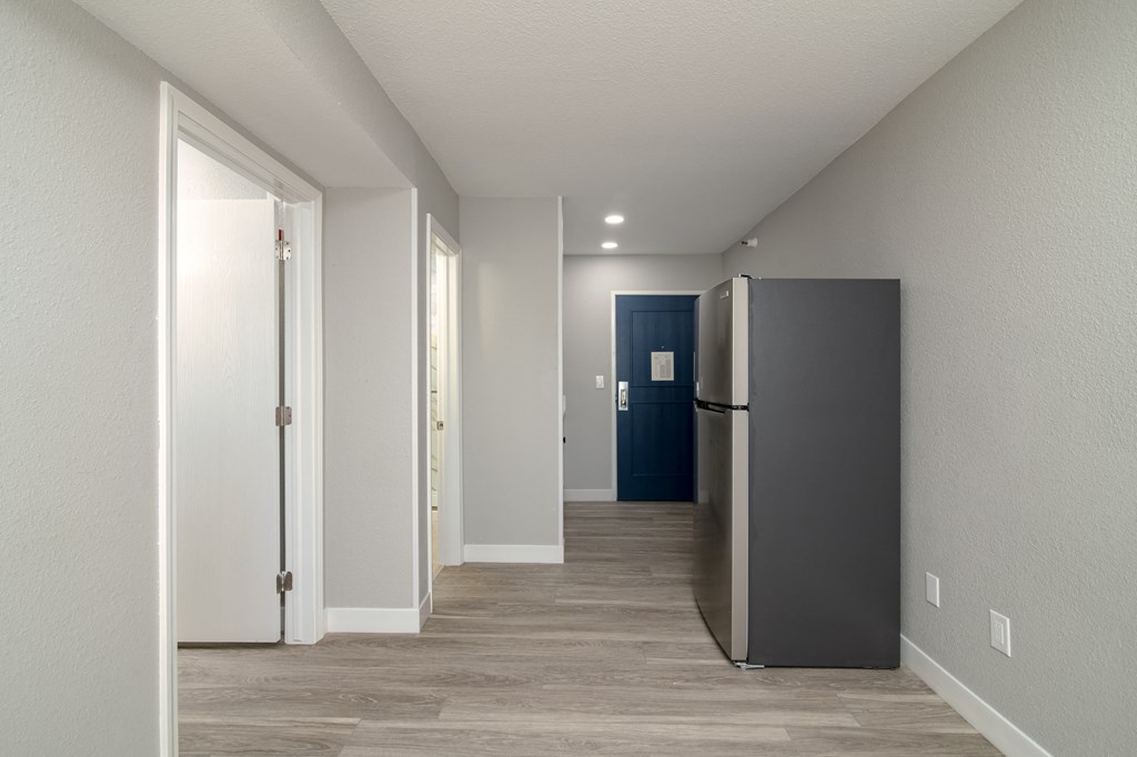 a room with a refrigerator and a hallway with a blue door