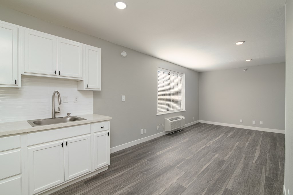 an empty kitchen and living room with white cabinets and a sink
