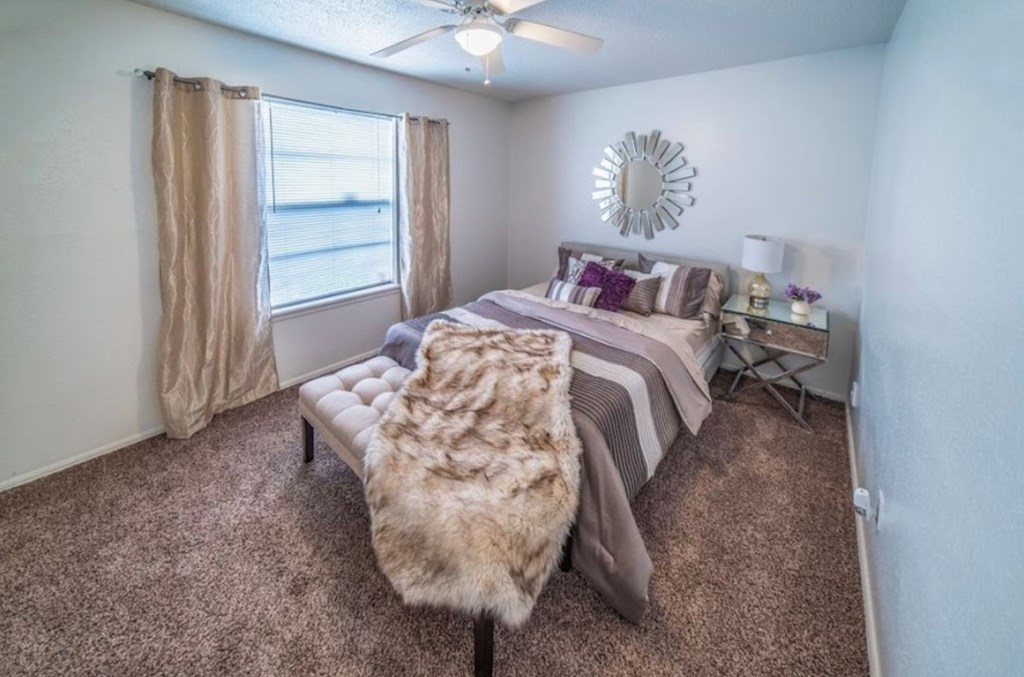 A bedroom with a bed, a bench, and a window with curtains.