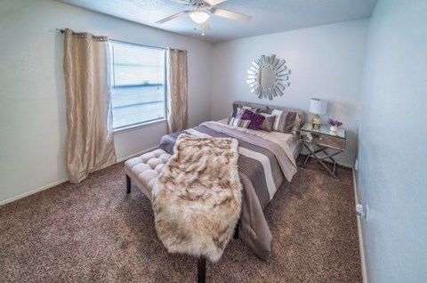 A bedroom with a bed, a bench, and a window with curtains.
