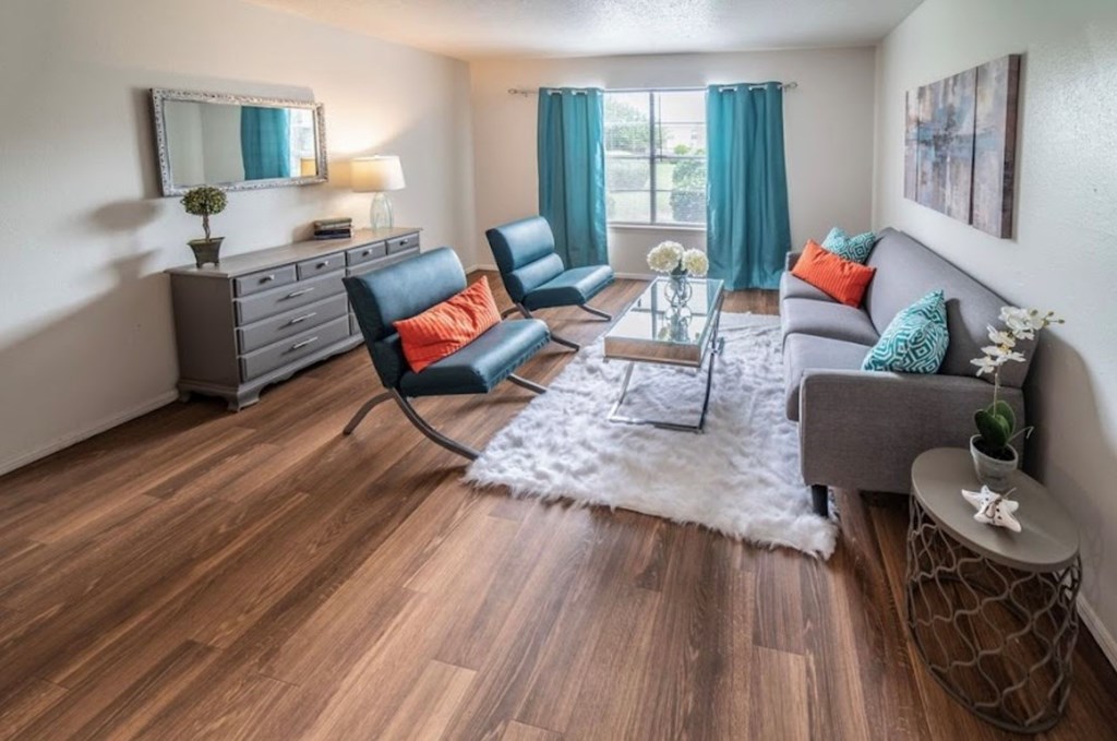 A living room with a grey couch, a black chair, and a wooden floor.