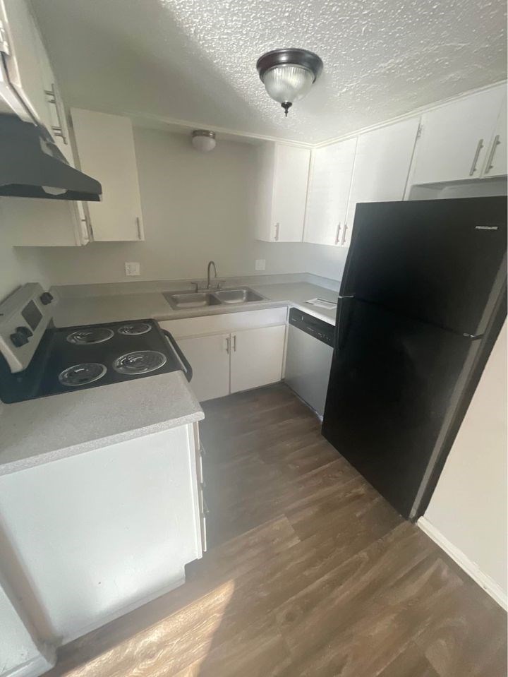 A black refrigerator stands in a kitchen with white cabinets and a black stove.
